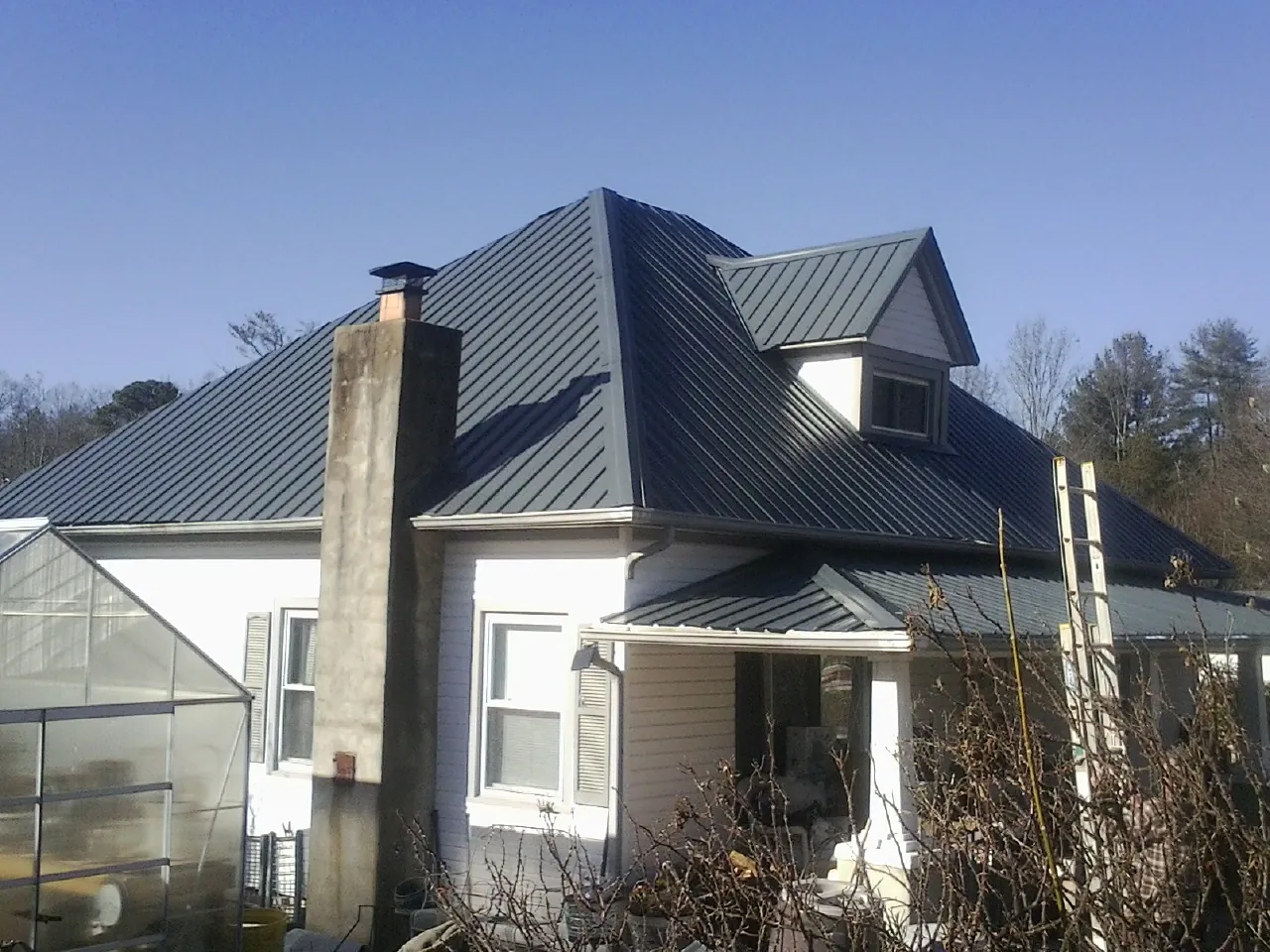 Dark blue standing seam metal roof on a white farmhouse with dormer — Slate & Tile Roof Repair by Roofing Brothers in Elk Park
