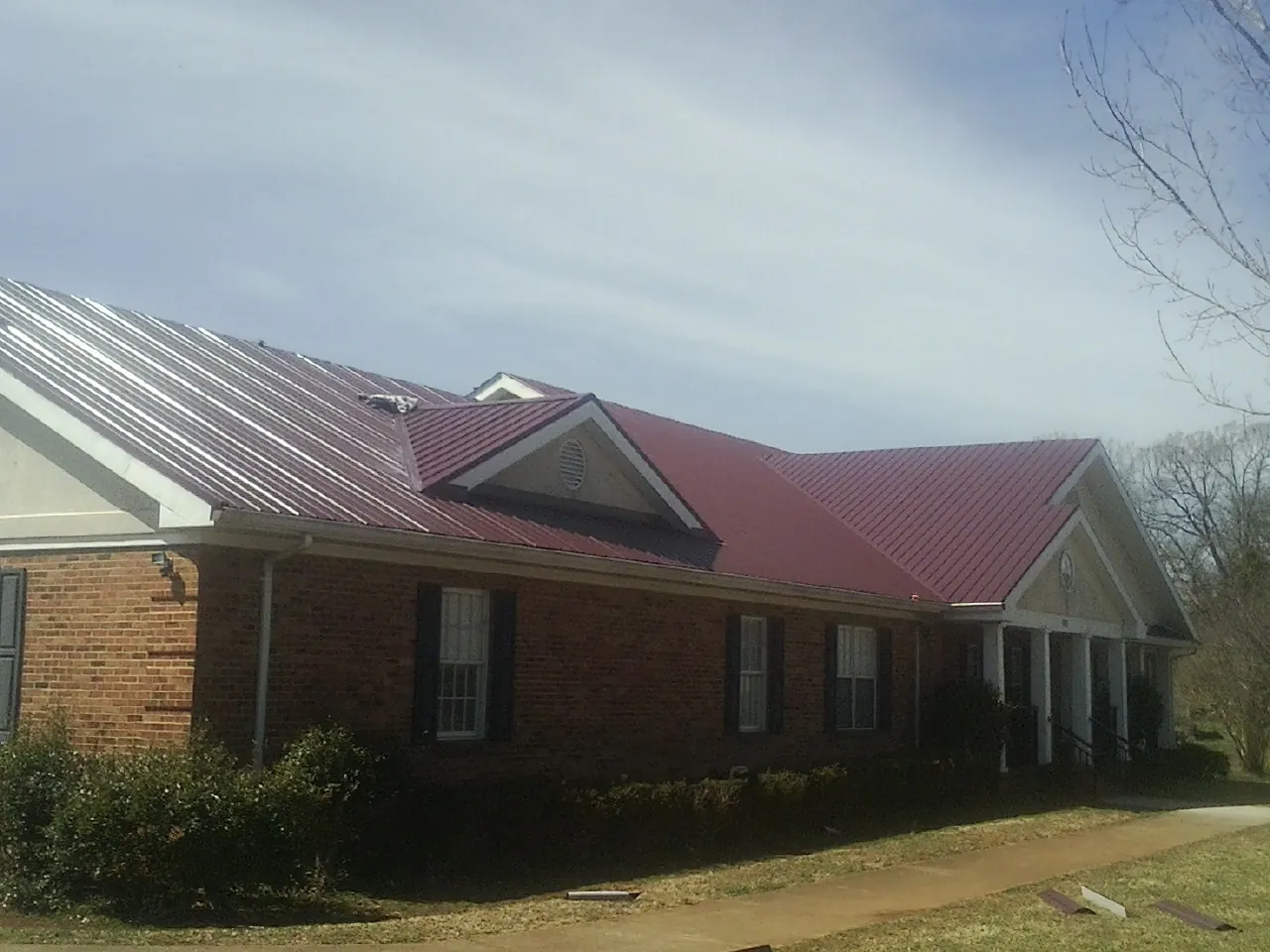 Red metal roof with gabled entries on a long brick building, from a Hail Damage Roof Repair job in Elk Park