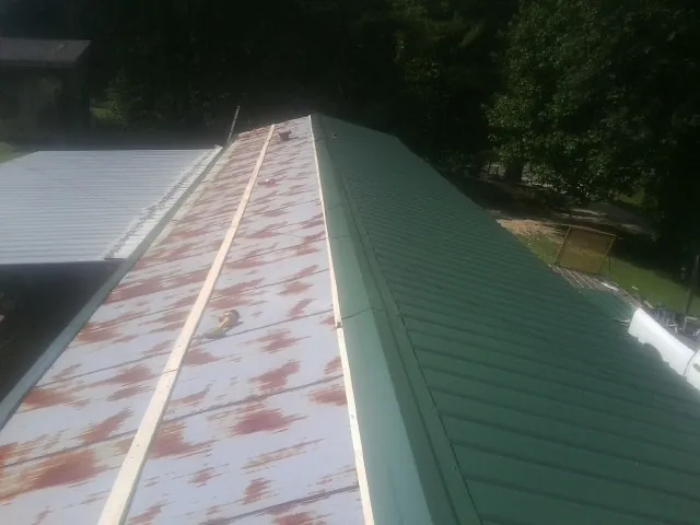 Old rusted panels beside newly installed green metal roofing — Wind Damage Roof Repair by Roofing Brothers in Elk Park