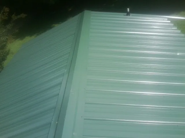 New green metal panels meeting at the ridge of a roof — Flat Roof Repair work by our crew in Elk Park