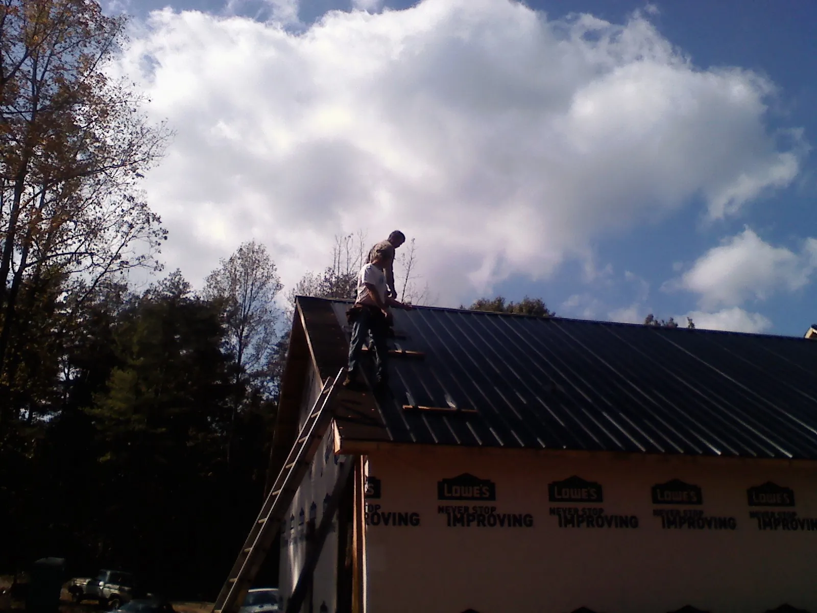 Roofer fastening dark metal panels high against a cloudy sky, from a Roof Inspection job in Elk Park