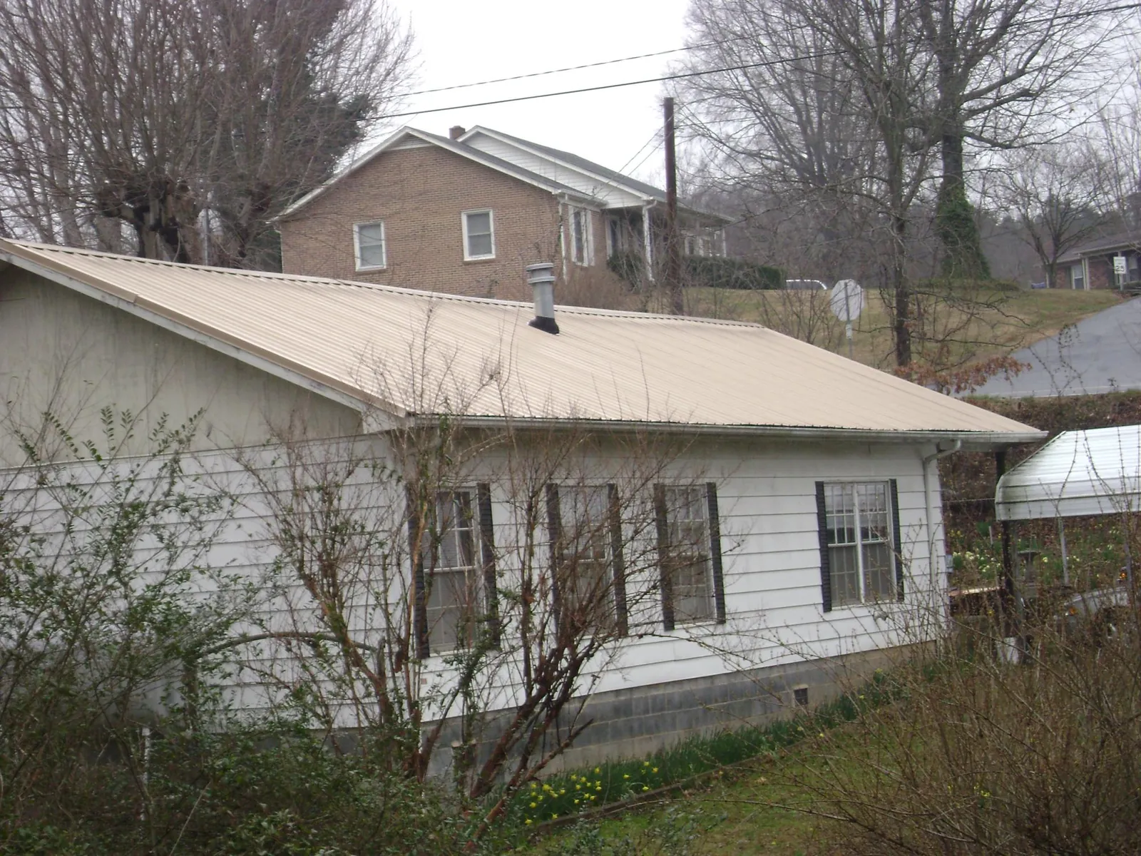Tan metal roof on a white sided house set into a hillside — Commercial Roofing by Roofing Brothers in Elk Park