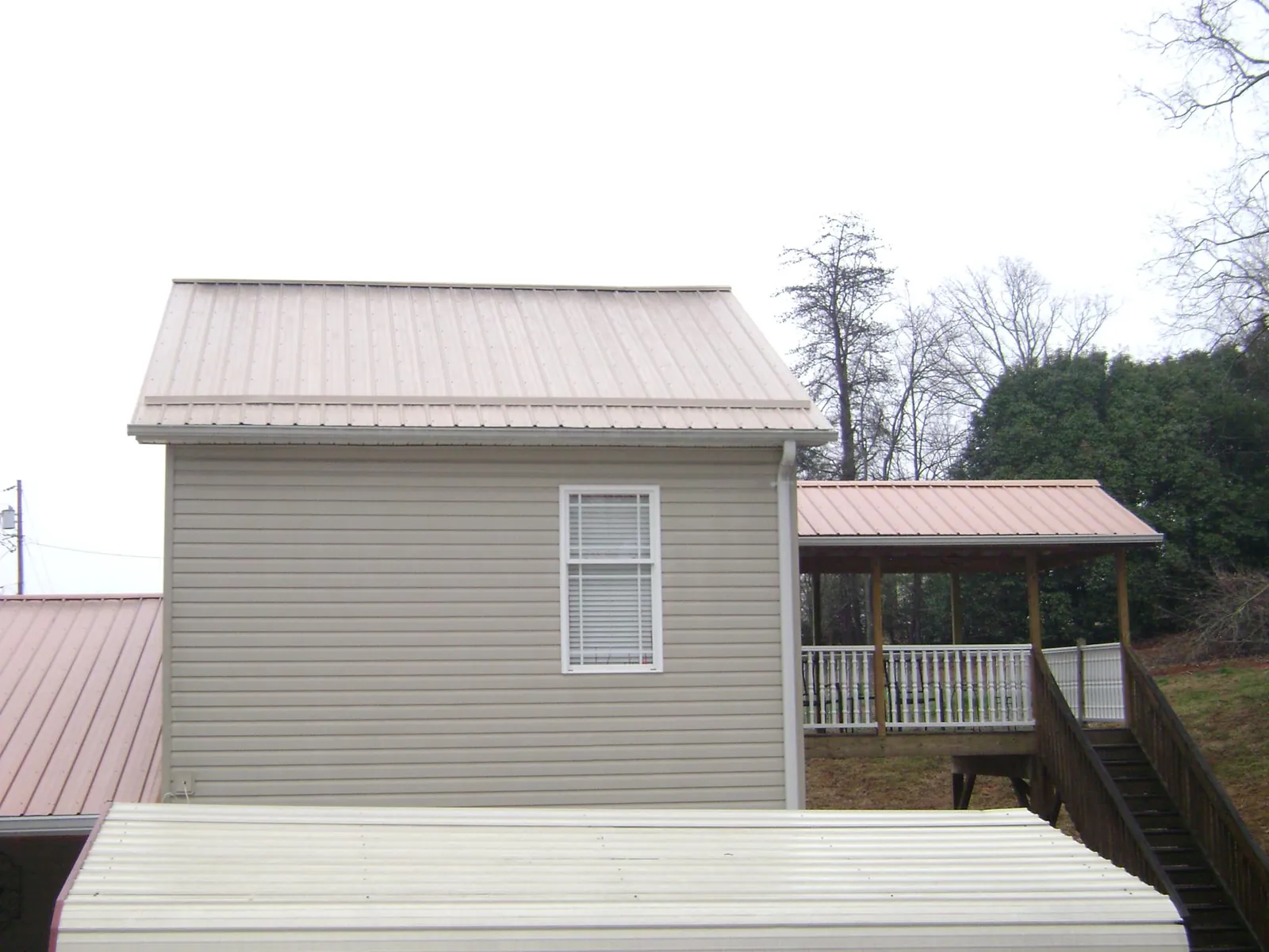 Tan metal roofs on a two story addition and attached porch, from a Roof Replacement job in Elk Park